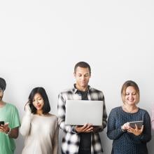 Group of people standing in a line holding technology devices.